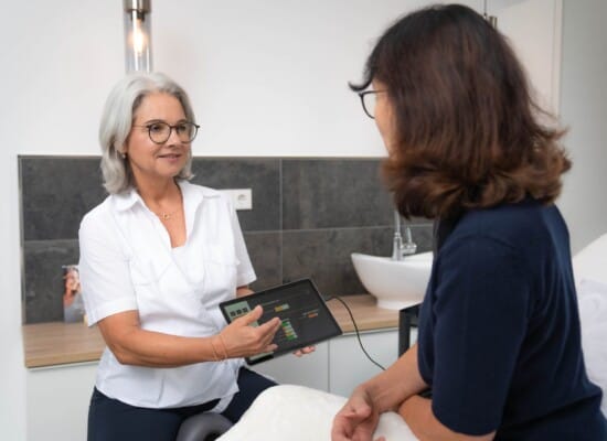 Kosmetikerin hält das Tablet mit den Messergebnissen in der Hand und erklärt die Daten einer Kundin