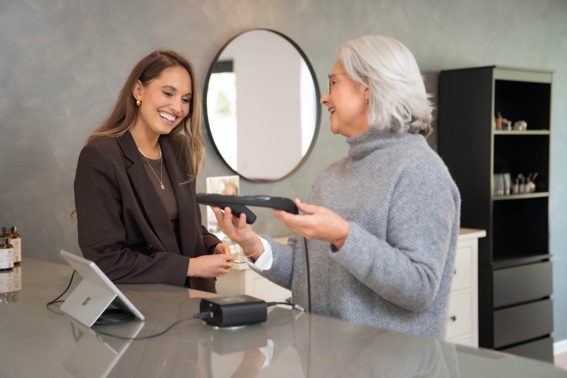 Kosmetikerin hält das Beauty-Check Gerät in der Hand und erklärt es einer Kundin.