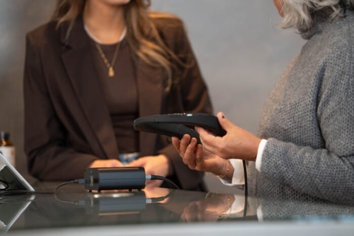 Kosmetikerin hält Messergerät in der Hand und erklärt einer Kundin die Funktionsweise