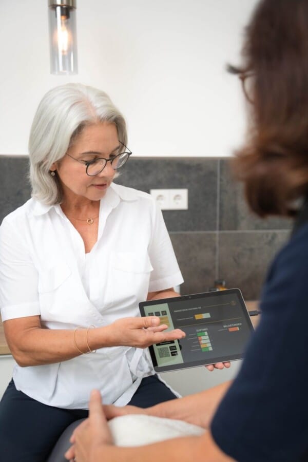 Kosmetikerin hält das Tablet mit den Messergebnissen in der Hand und erklärt die Daten einer Kundin